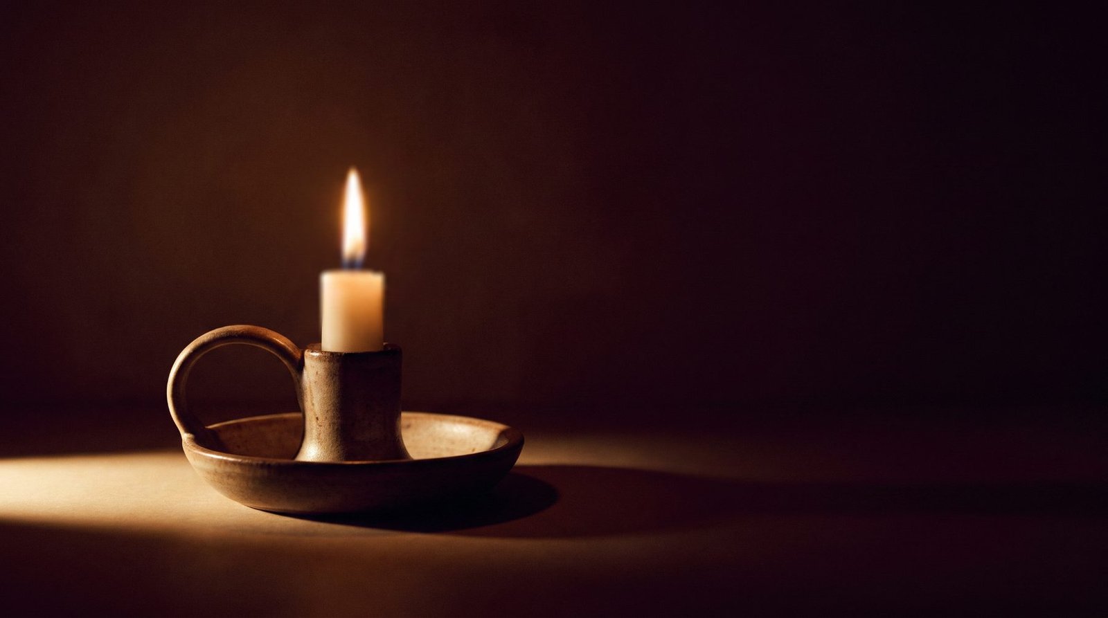Een brandende kaars in een eenvoudige keramieken houder, warm licht tegen een donkere achtergrond